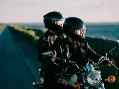 Coppia in moto romantica, con caschi neri, giacche di pelle, su una strada panoramica al tramonto.