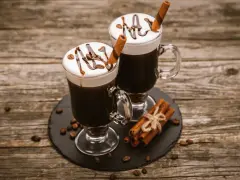 Dwa Irish coffee z bitą śmietaną, polewą czekoladową i laską cynamonu. Jaki to smak? Słodki, kawowy, z nutą alkoholu i przypraw.