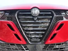 Czerwona Alfa Romeo z bliska. Widoczny grill w kształcie tarczy z logo, reflektory i detale karoserii w zbliżeniu. Alfa makro.