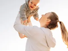 Mutter wirft ihr lachendes Baby in die Luft. Ein fröhlicher helikopter-mutter test im Freien.