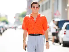 Hombre con camisa naranja estampada y pantalones grises, luciendo un elegante french tuck.