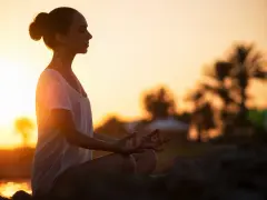 Frau meditiert im Sonnenuntergang. Ein kurzer 5-Minuten-Meditations-Text könnte hier perfekt passen, um diese friedliche Szene zu vertiefen.