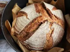 Ein frisch gebackenes Sauerteigbrot mit knuspriger Kruste liegt in einem Gusseisentopf. Perfekt für jedes Sauerteigbrot Rezept.