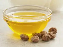 Huile dorée dans un bol en verre, entourée de noix de terre. Découvrez les noix de terre bienfaits pour une peau éclatante et une santé optimale.
