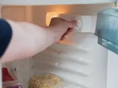 Main tenant ajuste la température pour un congélateur. On voit des aliments congelés.