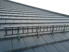Metalowa drabinka śniegowa na ciemnej dachówce karpiówce w łuskę.