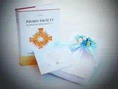 Dedykacja na komunię: Pismo Święte, ozdobna kartka i prezent z błękitną wstążką i kwiatami.