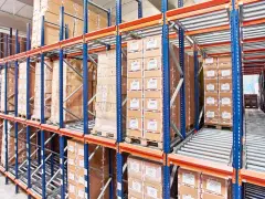 Magazyn z kartonami na regałach typu flow rack. Towary przesuwają się po rolkach, ułatwiając kompletację.