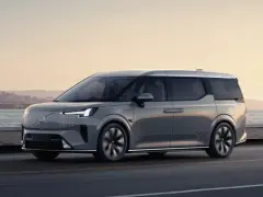 Szary Volvo EM90 jedzie wzdłuż wybrzeża o zachodzie słońca.