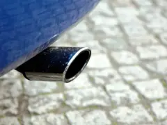 Il tubo di scarico cromato di un'auto blu, parte del silenziatore che attutisce il rumore del motore, su un selciato.