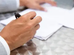 Dłoń z długopisem nad dokumentem, przygotowująca się do podpisania umowy przyrzeczonej.