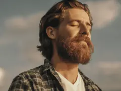 Homme à la barbe rousse, yeux fermés, profitant du soleil. Une image qui évoque le bien-être et la vitalité, peut-être liée à un test libido homme.
