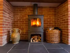 Estufa de leña con fuego encendido, chimenea de ladrillo, leña en cesta y jarrón. Guía para como instalar una estufa de leña con salida horizontal.