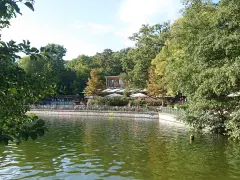Grüne Bäume säumen den Schlachtensee Berlin, wo Menschen auf der Terrasse eines Restaurants sitzen.