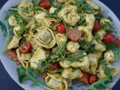 Ein köstlicher Tortellini-Salat mit Pesto, Kirschtomaten und Mozzarella-Kugeln, garniert mit Rucola.