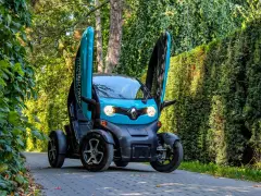 Niebieski Renault Twizy z otwartymi drzwiami stoi na ścieżce wśród zieleni.