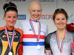 Joanna Rowsell, a bald cyclist in a white and red jersey, smiles on the podium with two other medalists.