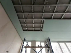 Instalación de falso techo de pladur para insonorizar habitación de ruidos de vecinos. Andamio y estructura metálica visibles.