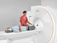 Pacjent leży na łóżku rezonansu magnetycznego, a technik przygotowuje jego nogi do badania. To właśnie mri co to za badanie, które pozwala zajrzeć do wnętrza ciała.