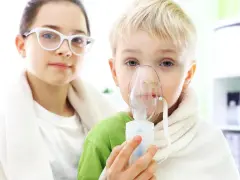 Dziecko z maską inhalatora, obok dziewczynka w okularach.