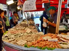 Mercato del pesce a Venezia: bancarelle piene di pesce fresco, gamberi e calamari. Un venditore serve i clienti.