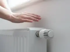 Dłoń nad grzejnikiem, sprawdzająca ciepło. Rozpoczyna się sezon grzewczy, czas na komfortowe ogrzewanie.