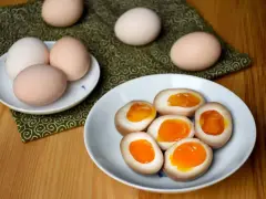 Na talerzu leżą połówki jajek do ramenu z płynnym, pomarańczowym żółtkiem. Obok całe jajka.
