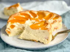 Ein saftiger Pfirsichkuchen mit cremiger Füllung und frischen Pfirsichspalten. Ein Stück wird gerade mit einem goldenen Tortenheber herausgehoben.