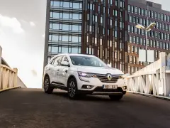 Biały Renault Koleos na tle nowoczesnego budynku. Czy warto zainwestować? Sprawdź interrisk opinie.