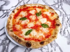 Pyszna pizza neapolitańska z pomidorami, mozzarellą i bazylią, z charakterystycznie wyrośniętym brzegiem.