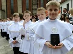 Chłopcy w białych albach, gotowi do komunii, trzymają modlitewniki. Jeden z nich uśmiecha się do aparatu.