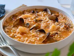 Un delicioso arroz caldoso de marisco, repleto de gambas, mejillones y almejas, servido en un cuenco blanco.