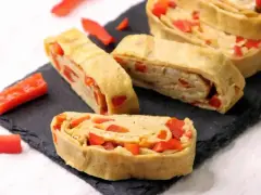 Roladki z jajek z papryką, przypominające omlet do sushi, ułożone na czarnej desce.