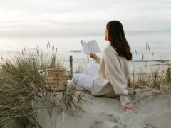 Kobieta czyta książkę na plaży, ciesząc się spokojem i świeżym powietrzem. To idealny moment, by poczuć, kiedy jest najwięcej jodu nad morzem.