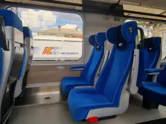 Wygodne, niebieskie fotele w wagonach PKP Intercity bez przedziałów. Widok na mijany krajobraz i inne wagony.