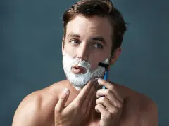 Hombre con espuma de afeitar en la cara, aprendiendo como afeitarse la barba con una maquinilla.