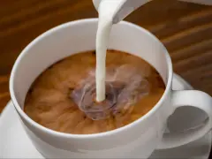 Biała filiżanka kawy, do której wlewane jest mleko. Zastanawiasz się nad mleko owsiane kcal?