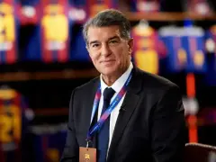 Uśmiechnięty prezes Barcelony, Joan Laporta, w garniturze, z identyfikatorem FC Barcelona na szyi.