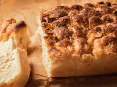 Chrupiąca, złocista włoska focaccia z oliwkami i ziołami, z apetycznie odłamanym kawałkiem.