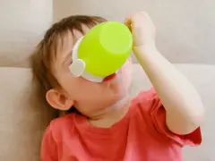 Małe dziecko pije z zielonego kubka niekapka LOVI.