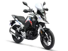 Nowy motocykl gotowy do docierania. Biało-czarny z czerwono-niebieskimi akcentami, z wysoką szybą i terenowymi oponami.