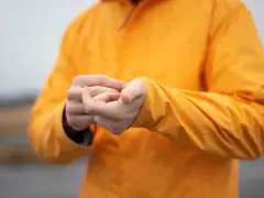 Persona se frota las manos dentro de una chaqueta naranja brillante. El poliéster da calor y protege del frío.