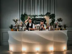 Dwóch barmanów przygotowuje drinki przy nowoczesnym, podświetlanym barze. To idealny drink bar na wesele, oferujący orzeźwiające napoje.