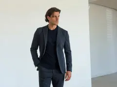 Uomo con giacca e pantaloni grigi, una mano nella tasca laterale del pantalone, mostrando i diversi tipi di tasche pantaloni uomo.