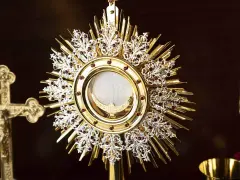 A golden monstrance holds the blessed sacrament, surrounded by ornate details and red jewels. A crucifix stands nearby, a symbol for a blessed sacrament prayer request.