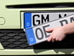 Dłoń trzyma niemieckie tablice rejestracyjne z literami "OE" i "GM".