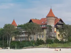 Elegancki hotel z wieżą i czerwonym dachem, otoczony drzewami, idealny na łeba atrakcje dla dorosłych.