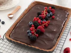 Tarta de chocolate cremosa decorada con frutos rojos frescos: frambuesas, moras, arándanos y grosellas.