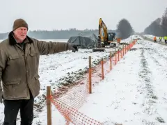 Mężczyzna wskazuje na plac budowy drogi. W tle koparka i pracownicy. Zima i specustawa drogowa utrudniają prace.