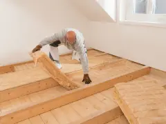 Mann verlegt Dämmmaterial auf Holzbalkendecke, vorbereitend für Estrich.